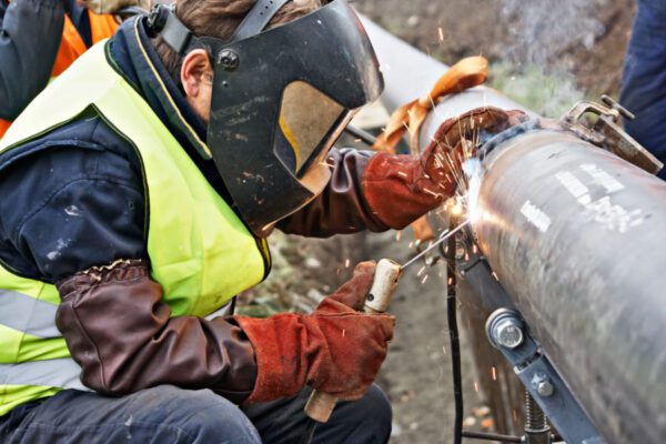 Man welding gas pipeline in protective gear.