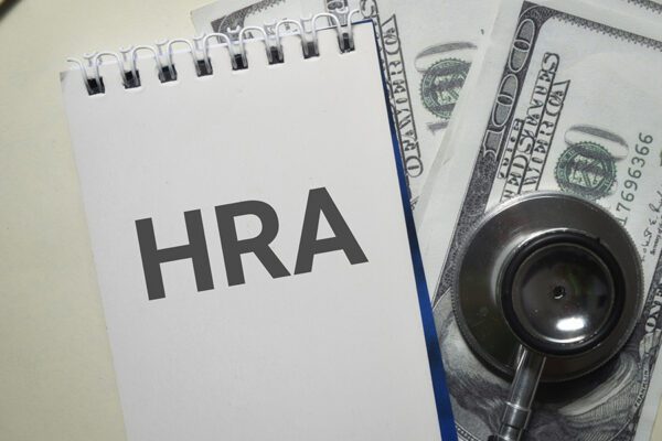 A photo of a notepad with the words "HRA" typed out, accompanied by a stethoscope and two hundred dollar bills.