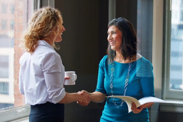 Two employees shaking hands. One employee is carrying a folder with files.