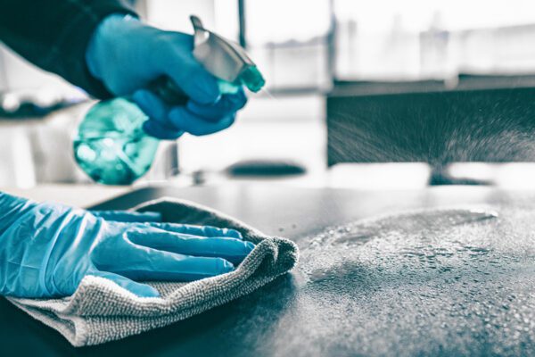 Photo of hands with rubber gloves spraying cleaner and wiping down the kitchen countertop.