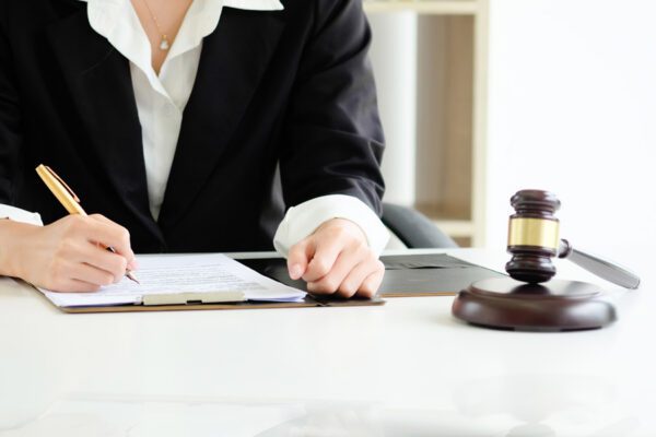 A woman writing on a legal pad with a gavel next to her.
